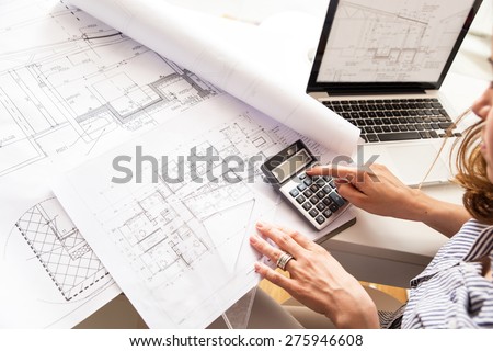 Female architect working at home.She looking blueprints.