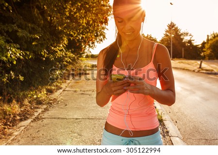 Female jogger running and listening to music on her smart phone.Sunset and lens flare effect.