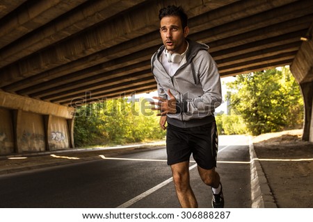 Jogger running in city environment.He wearing headphones around neck.