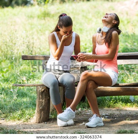 Two best female friends using smart phone and reading comments on social network.