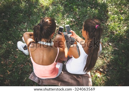 Two female friends sitting on grass and using smart phones.Image taken from above.