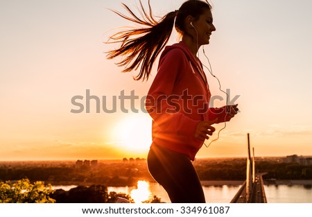 Female runner jogging on beautiful sunset. City scape in background.