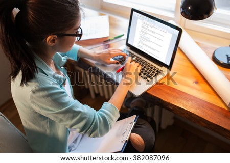 Young female blogger working at home.She sitting in her working room and typing something on laptop.
