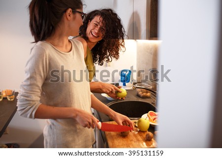 Young female friends in kitchen preparing together  vegetarian meal.Preparing fruit salad.Evening.