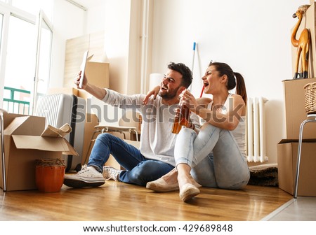Young couple moving in new home.Sitting on floor and relaxing after cleaning and unpacking.Doing selfie with tablet.