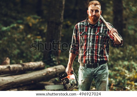 Lumberjack worker standing  in the forest with axe and chainsaw