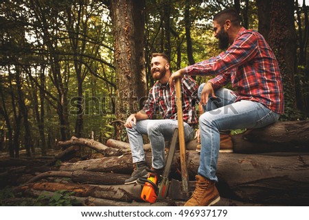 Two Lumberjacks sitting on wood pile and relaxing after hard work.Resting and talking.