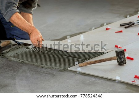 Ceramic Tiles. Tiler placing ceramic wall tile in position over adhesive with lash tile leveling system