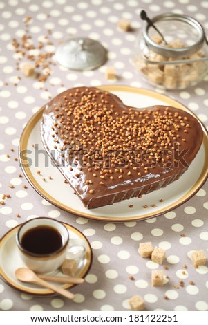 Chocolate Heart Cake with Chocolate Glaze and Caramelized Walnuts, with a cup of coffee and on a grey polka dot background.