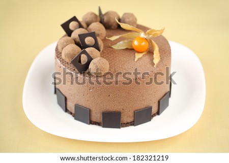 Chocolate Mousse Cake decorated with chocolate truffles, on a white plate, on a yellow background.