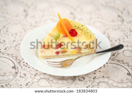 Piece of White Chocolate Cheesecake decorated with candied fruit on a white plate and light background.