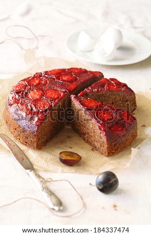 Upside-Down Plum Cake, on a baking paper, with silver knife, on a light background