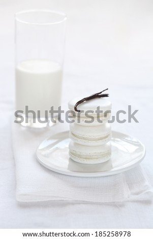 Vanilla Macarons on a white plate and white kitchen towel with vanilla bean and glass of milk; on a white background.