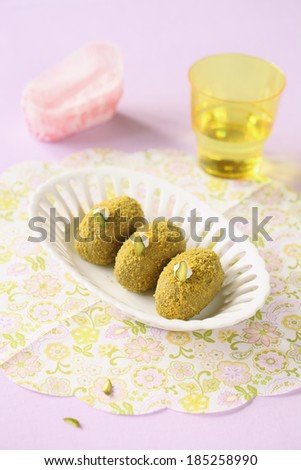 Pistachio Sweet Balls in a white vase for sweets and a glass of drink; on a light purple background.
