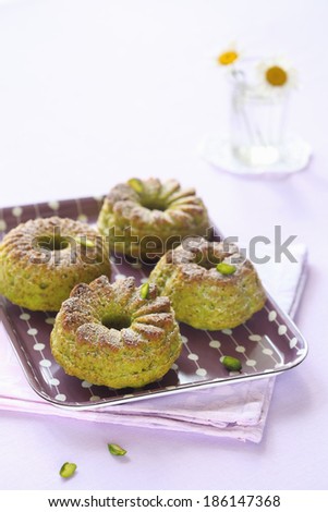 Pistachio Cakes on a purple plate and a kitchen towel, on a light purple background.
