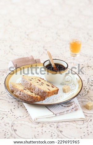 Two pieces of Earl Grey Loaf Cake with dried cranberries and raisins, and a cup of coffee on a white plate, on a light beige background.