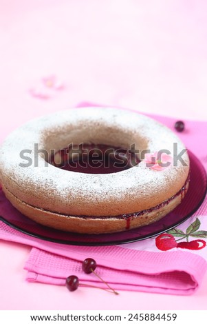 Simple Cake filled with Cherry Jam powdered with icing sugar on a plate and bright pink napkin.