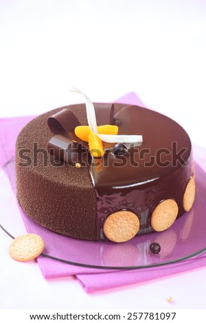 Milk Chocolate, Black Currant and Spiced Tangerine Entremet Cake coated with chocolate velvet spray and mirror glaze, decorated with chocolate elements and tangerine slices, on a purple napkin.