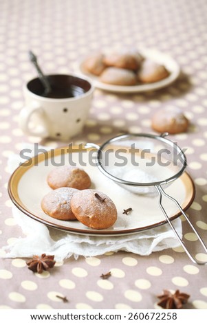 Vegan Spice Cookies on a plate, a flour sieve and a cup of coffee on a grey polka dot background.