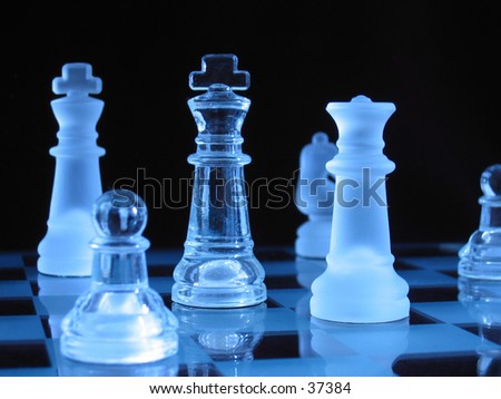 Glass chessmen during a play against dark background.