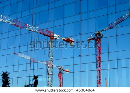 Three crane towers. White towers reflected in a blue glass backdrop.