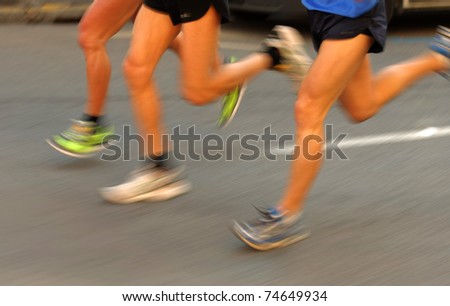 Marathon runners legs on the road followed by another runner with panning blur