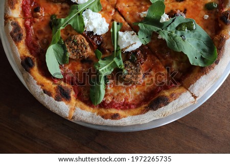 Italian Sausage and rocket salad pizza on wood background