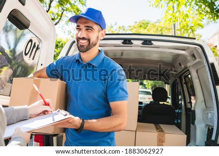 Delivery man carrying package while customer sign in clipboard.