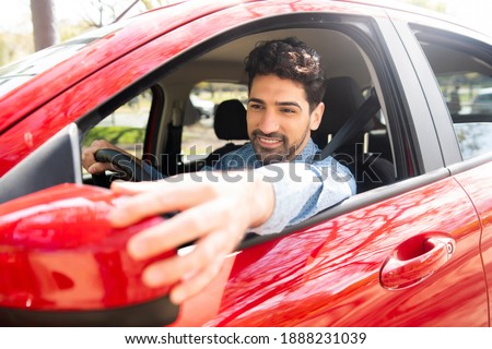 Man moving rear view wing mirror in car.