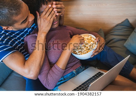 Latin couple watching a movie with laptop at home.