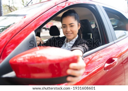 Woman moving rear view wing mirror in car.