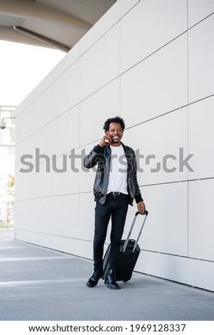 Tourist man talking on phone and carrying suitcase outdoors.
