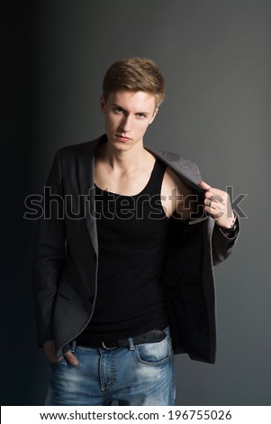 Young man in jacket and jeans standing on dark background