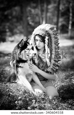 Indian woman in war bonnet playing with husky dog. Black and white