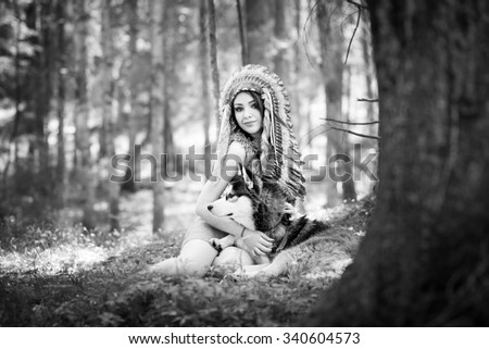 Indian woman in war bonnet playing with husky dog. Black and white