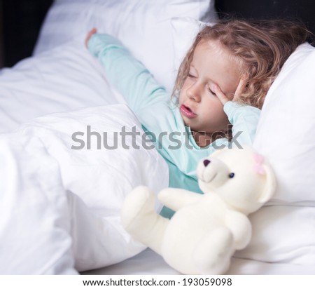 little girl stretches in bed with a toy bear