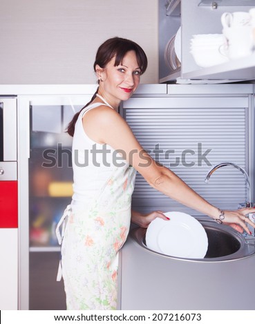 the girl apron washes the dishes in the sink