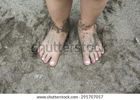 Little girl\'?s painted nail polish feet. Children\'s foot buried in the sand.