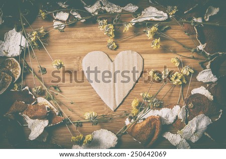 cardboard heart surrounded by a frame of dry citrus peel and withered flowers on a wooden table. vintage filter effects.