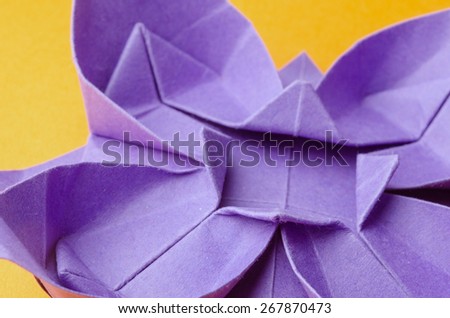 Abstract closeup of a purple paper origami flower on orange background. Side view.