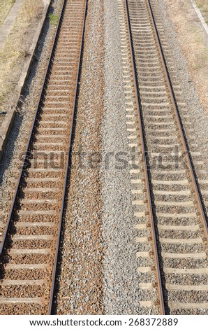two parallel railway tracks with two colored gravel and stones in between on a sunny day