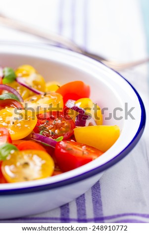 red and yellow cherry tomatoes salad in white bowl with onions, basil pepper and salt, on kitchen towel