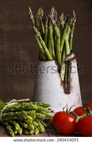 green asparagus in old tin can with tomatoes on brown background