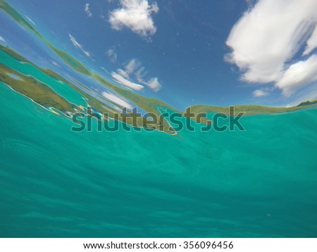 Underwater looking up towards the surface, with waves visible and blue sky and clouds reflected on the surface