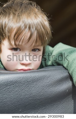 A young boy resting on black leather couch and looking in the camera