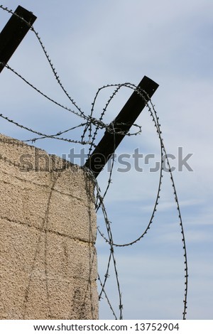 Barbed wire and steel posts atop a concrete wall.