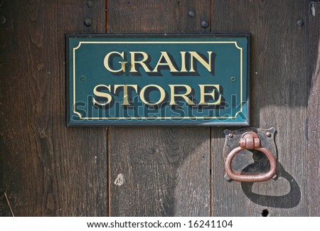A \'Grain Store\' sign with rusty door handle on an old wooden door.