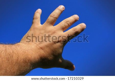 A male hand and forearm pointing skywards with fingers spread out and reaching. Set against a bright blue sky background.