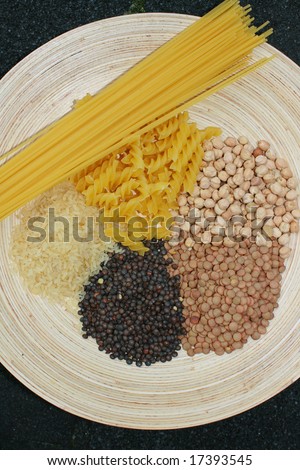 A selection of pulses on a wooden platter. Consisting of lentils, rice,spaghetti and chick peas.