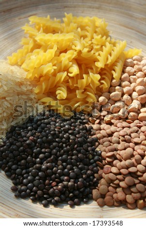 A selection of pulses and pasta set on a wood grained oval platter. Spaghetti,Lentils,Rice and Pasta.